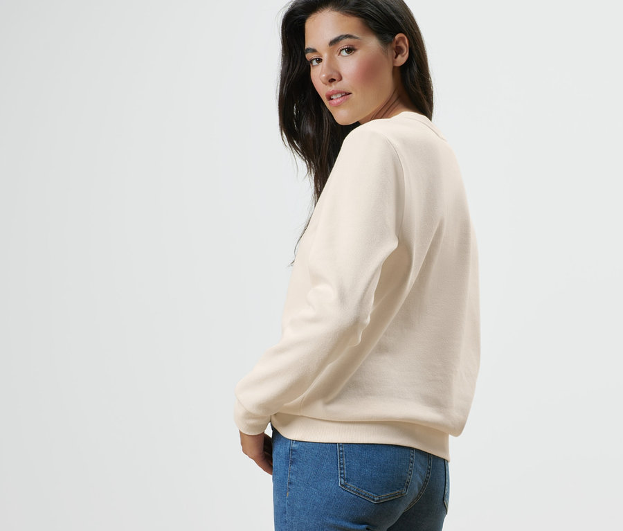 Frau blickt über die Schulter und posiert in einem Sweatshirt mit Print und Jeans.