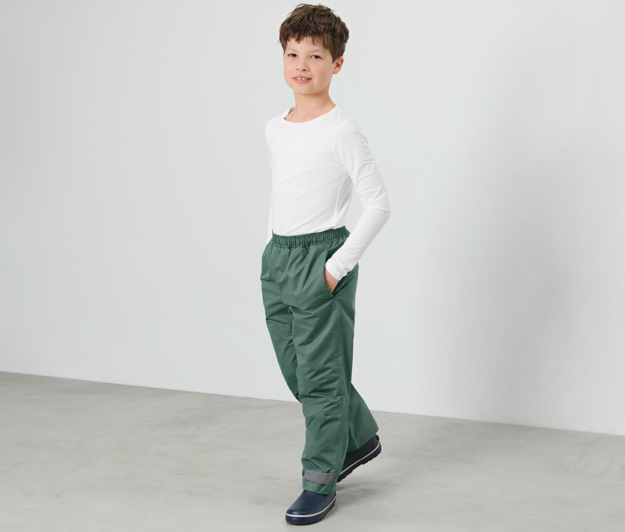 Ein Junge steht mit einer Hand in der Tasche seiner Kinder-Regenhose.