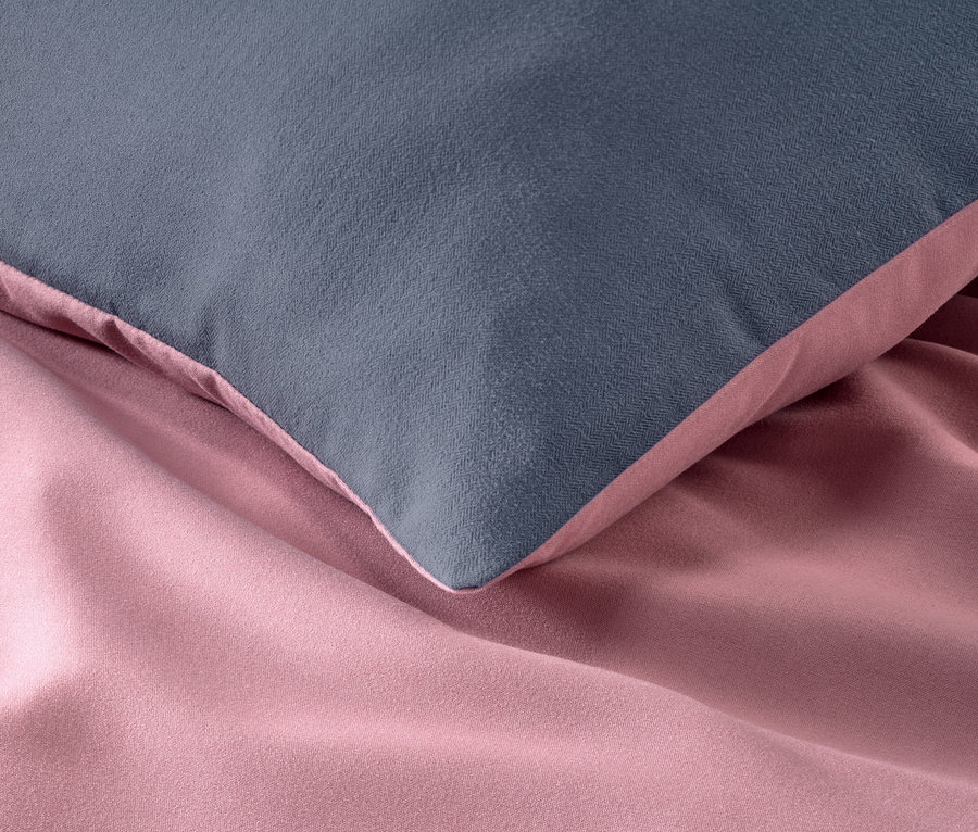 Detailaufnahme von grauem Kissen auf rosa Microfaser-Flanell-Bettwäsche.