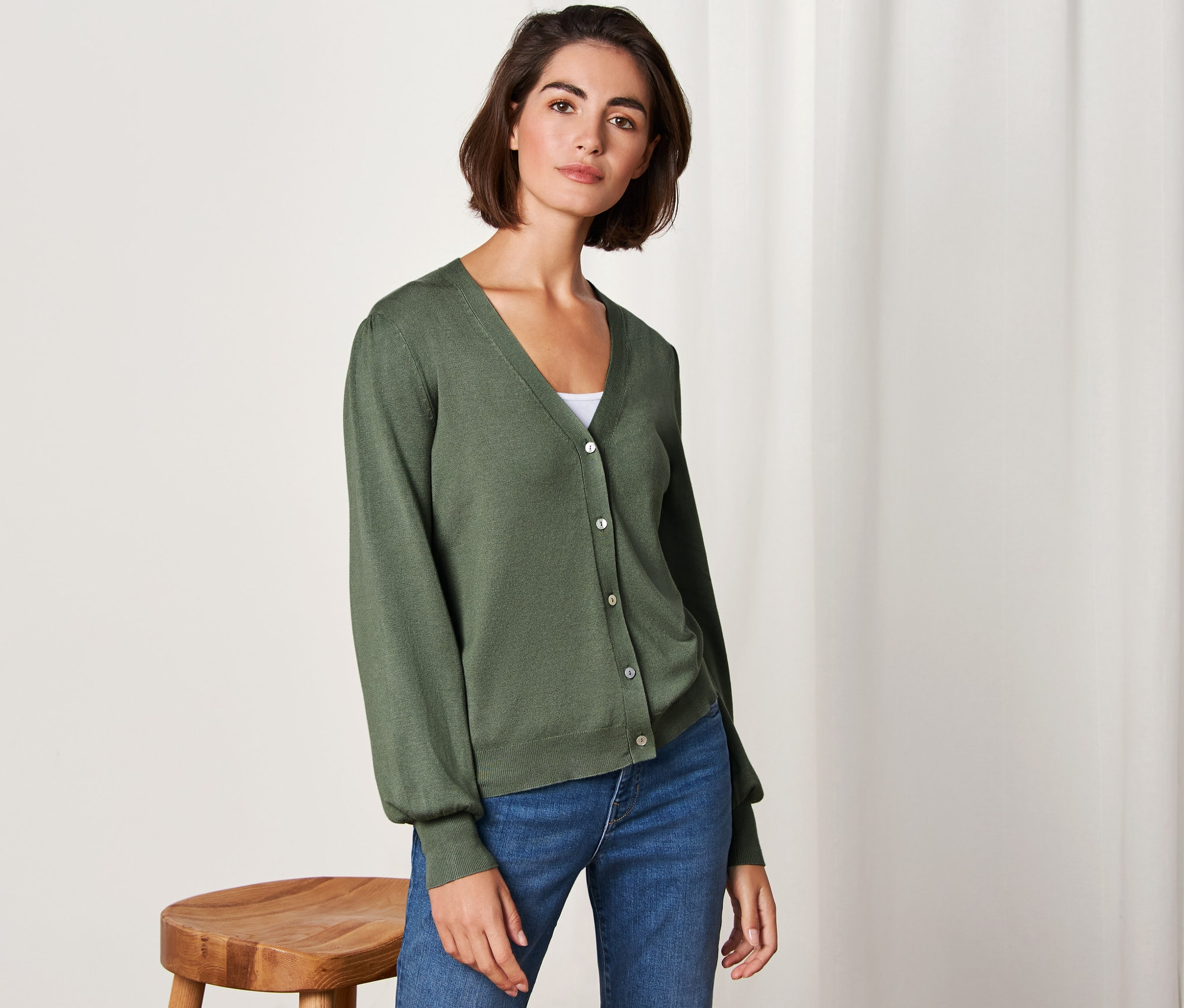 Frau posiert in einem grünen Feinstrick-Cardigan und Jeans.