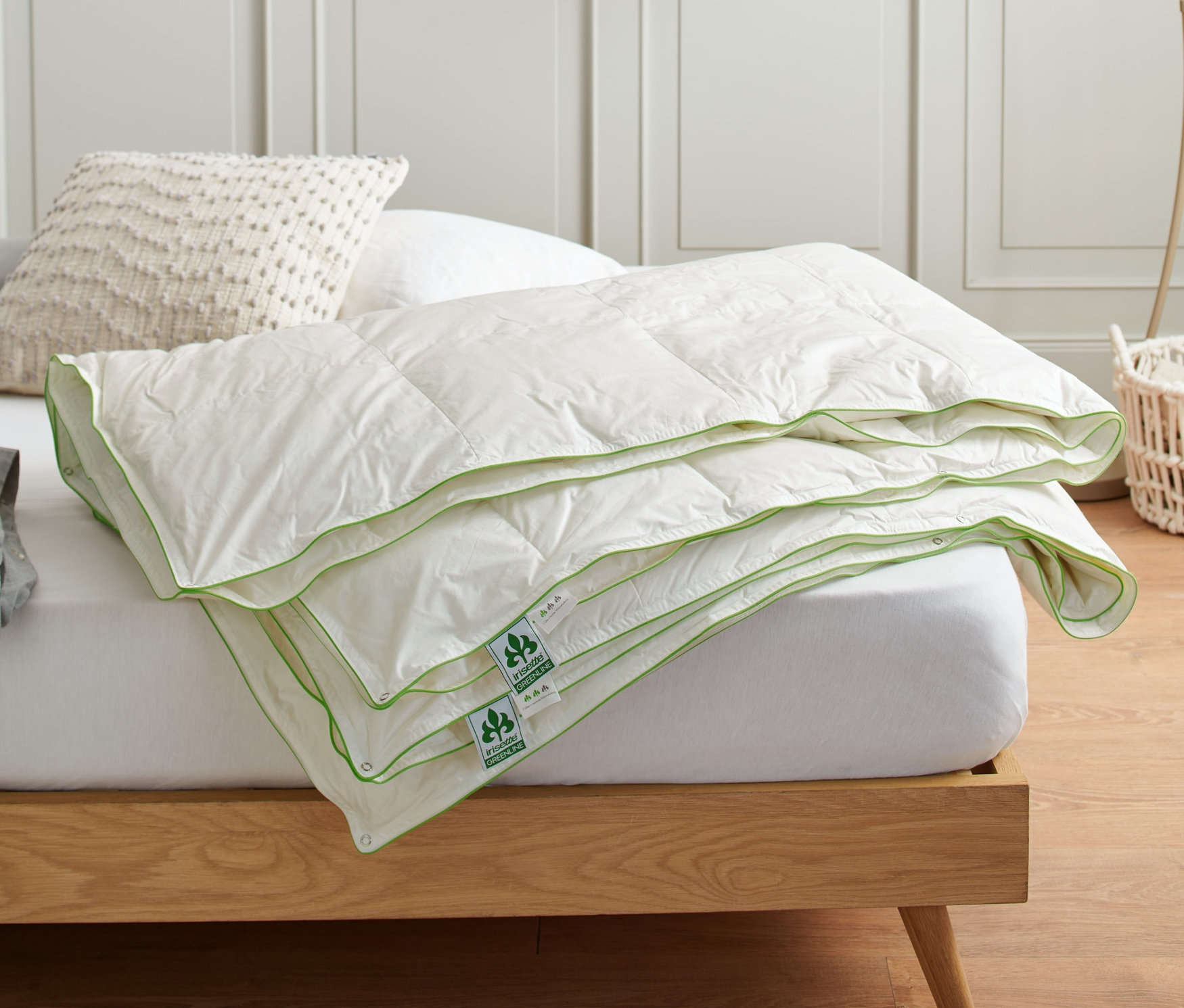 Eine gefaltete irisette® greenline 4-Jahreszeiten-Daunendecke in Normalgröße liegt auf einem Bett.