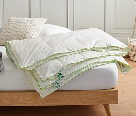 Eine gefaltete irisette® greenline 4-Jahreszeiten-Daunendecke in Normalgröße liegt auf einem Bett.