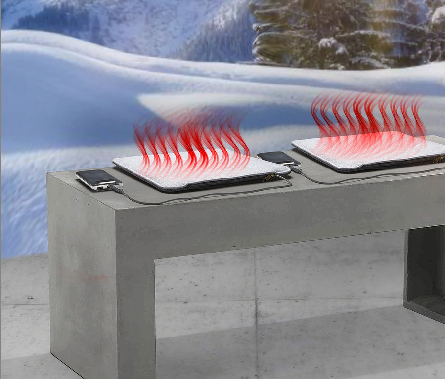 Zwei beheizbare Sitzkissen mit USB auf einer Betonbank, im Hintergrund verschneite Berge.