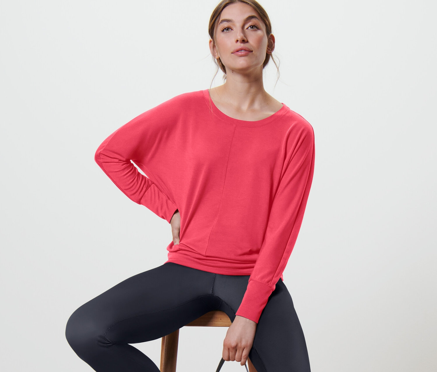 Frau sitzt auf einem Stuhl und trägt ein pinkes Sport- und Yogashirt.