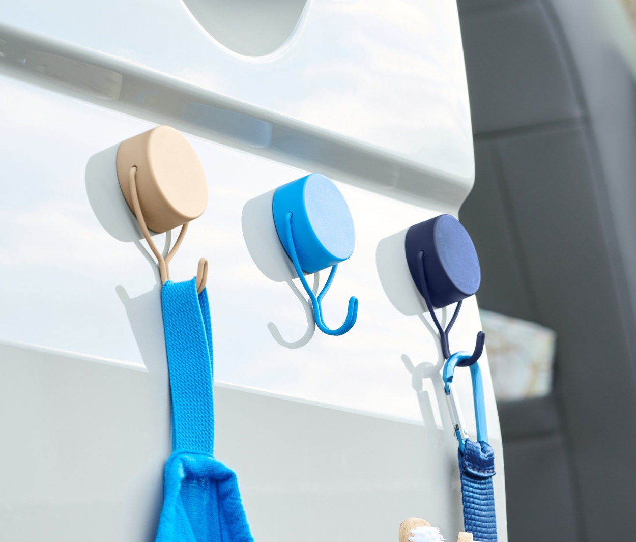 Drei Magnethaken halten ein blaues Handtuch und eine Toilettentasche an einer weißen Autotür.