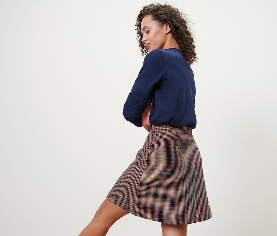 Frau posiert in kariertem Webrock und blauem Pullover.