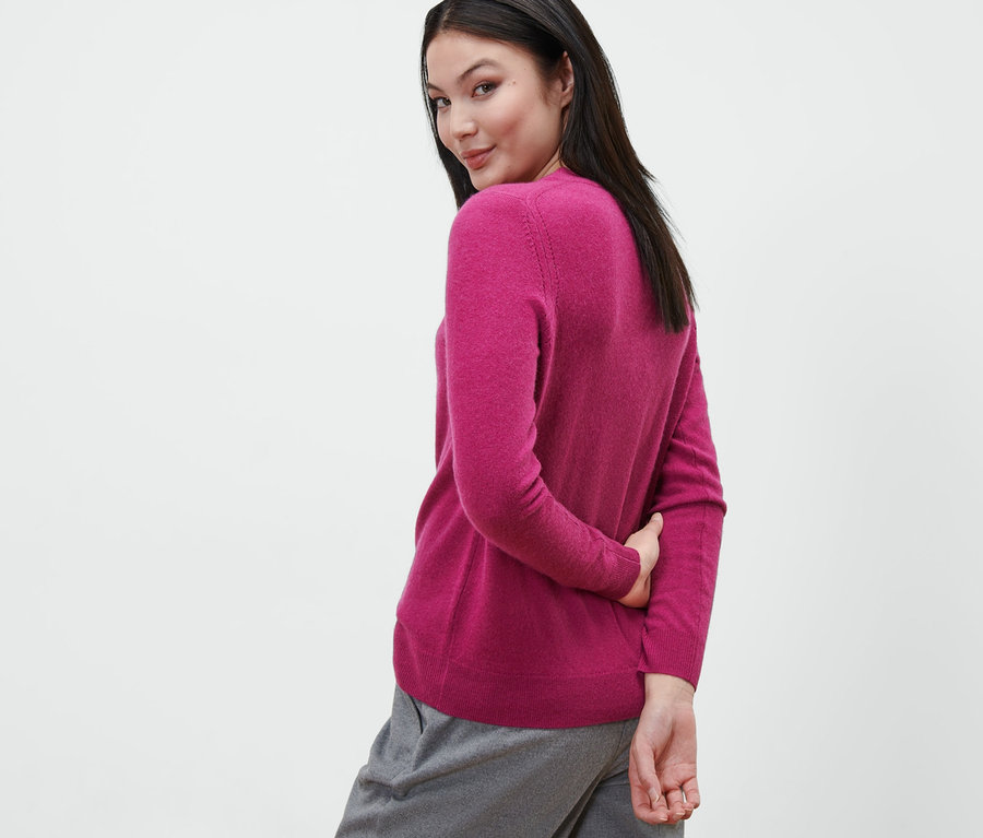 Frau blickt über die Schulter und trägt einen Feinstrickpullover mit Cashmere, berry, und graue Hosen.