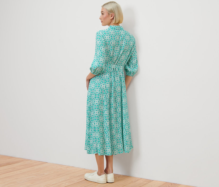 Frau steht mit dem Rücken zur Kamera und trägt ein Hemdblusenkleid mit Alloverprint.