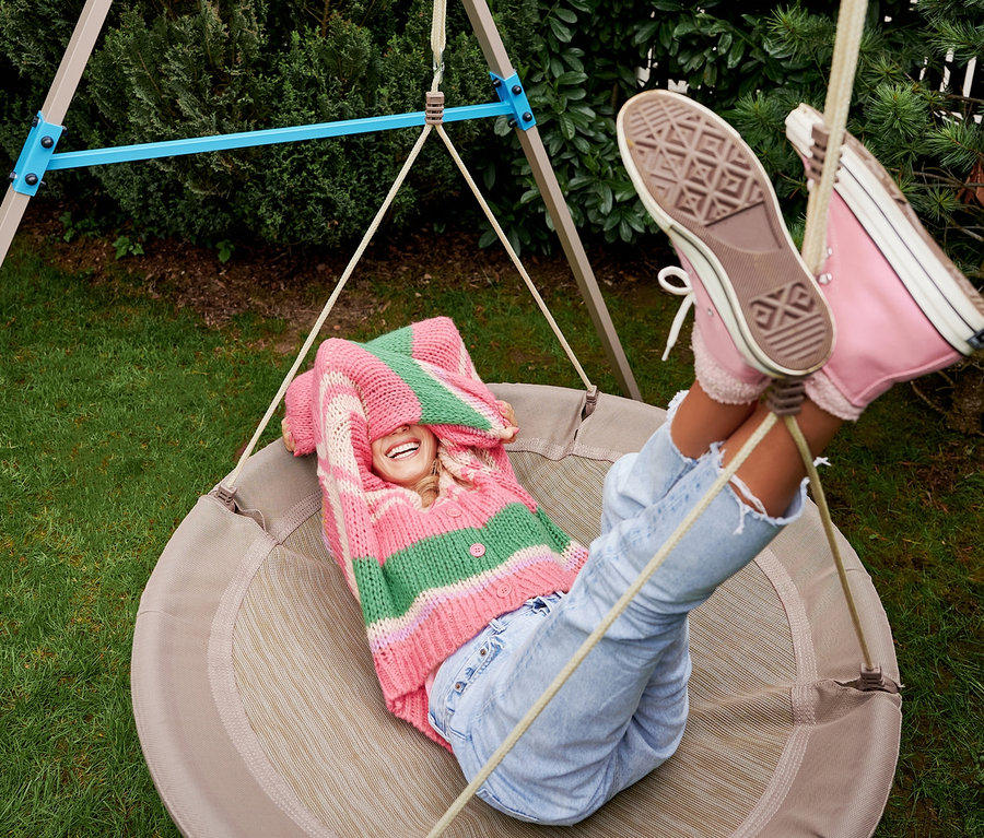 Eine Frau liegt in der beigen HUDORA Nestschaukel »Lounge«, Ø 110 cm und lacht.