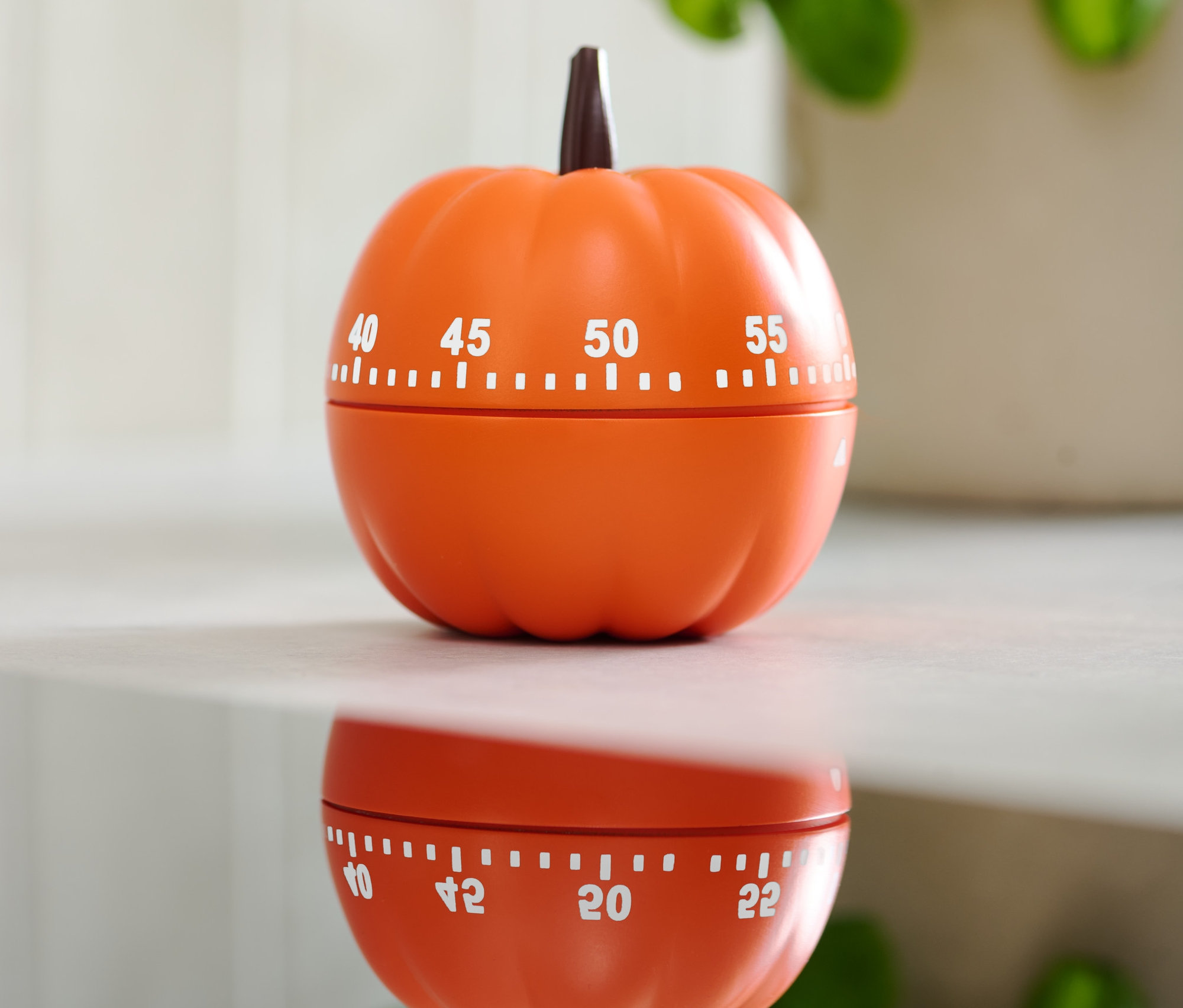 Orangefarbener Kurzzeitmesser in Kürbisform auf glänzender Oberfläche.