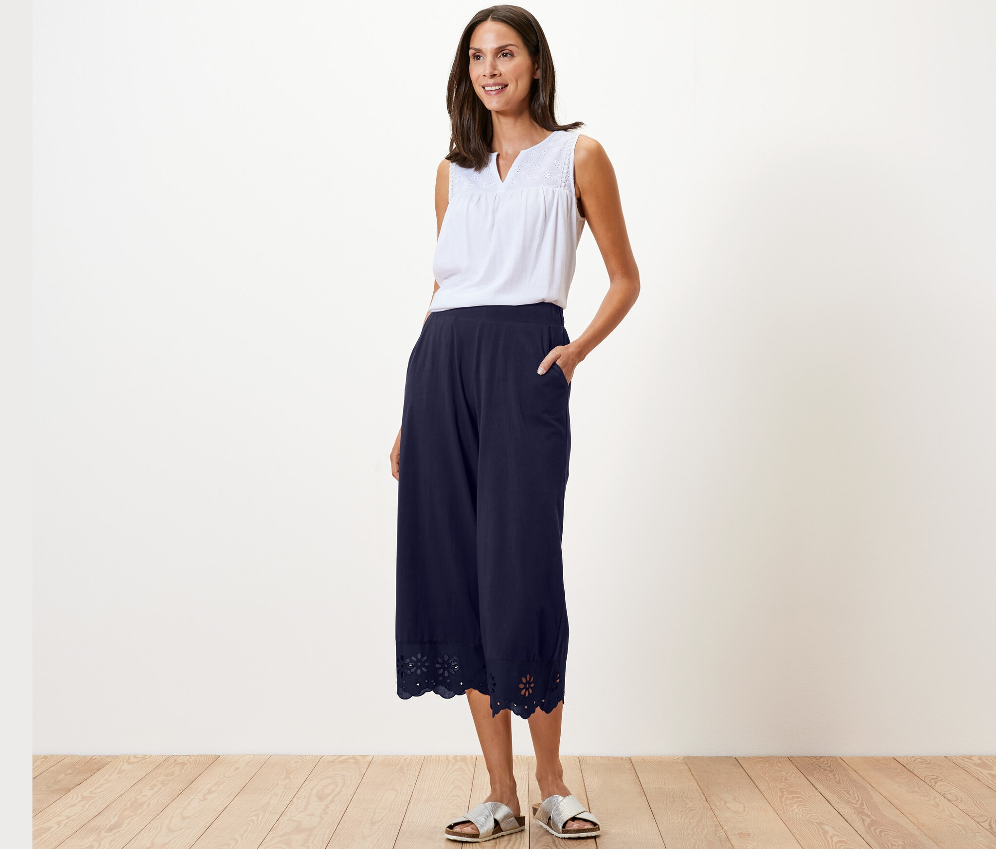 Frau posiert in weißem Top und marineblauer Culotte mit Stickerei.