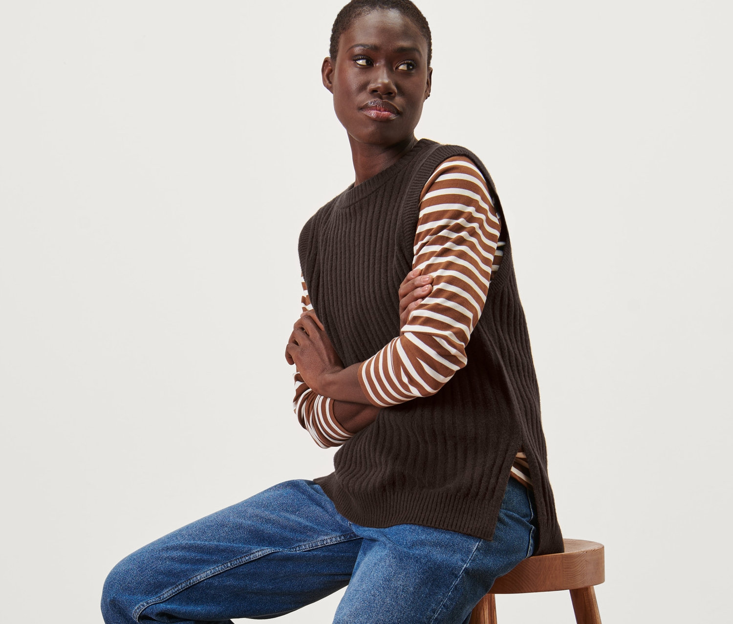 Frau sitzt auf einem Hocker und trägt einen Strick-Pullunder.