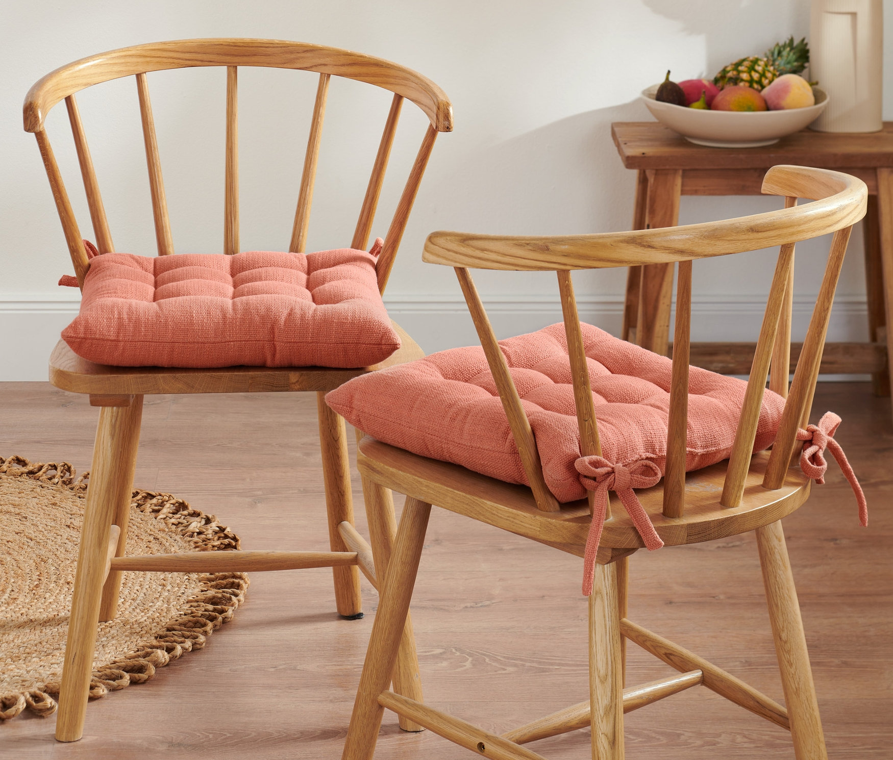 Zwei Holzstühle mit orangefarbenen Sitzkissen.