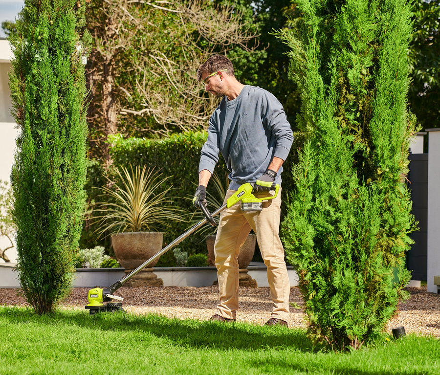 Mann trimmt Rasen mit RYOBI 18 V One+ Akku-Rasentrimmer mit Radführung.