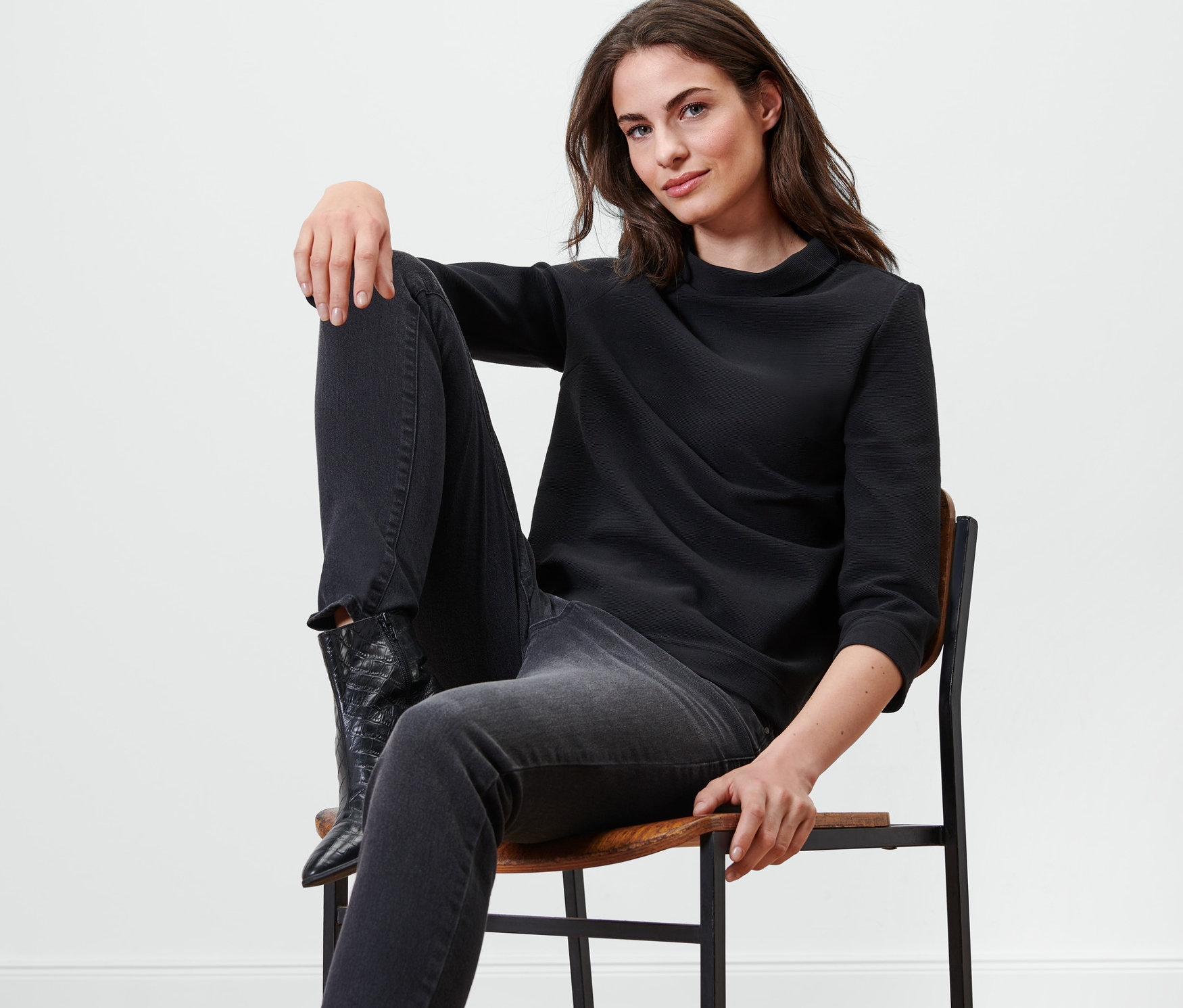 Frau sitzt auf einem Stuhl und trägt ein schwarzes Sweatshirt mit 3/4-Arm.