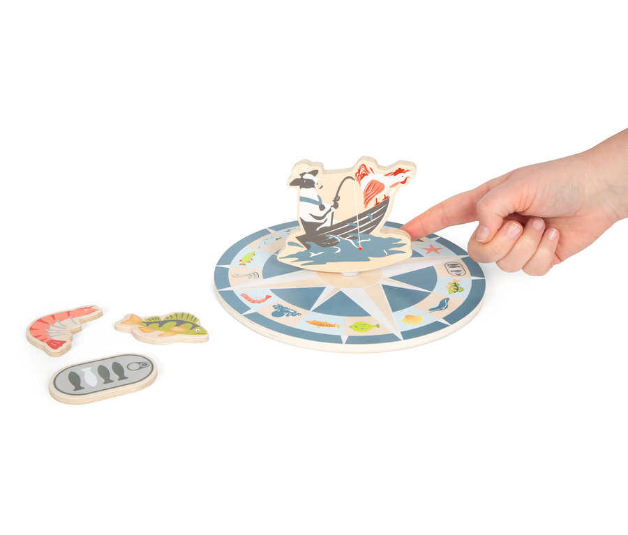 Eine Hand berührt ein Holzspielzeug mit einem Fischermotiv, daneben liegen eine hölzerne Garnele, ein Fisch und eine Konservendose. Zu sehen ist das Angelspiel »4 Friends« von small foot.