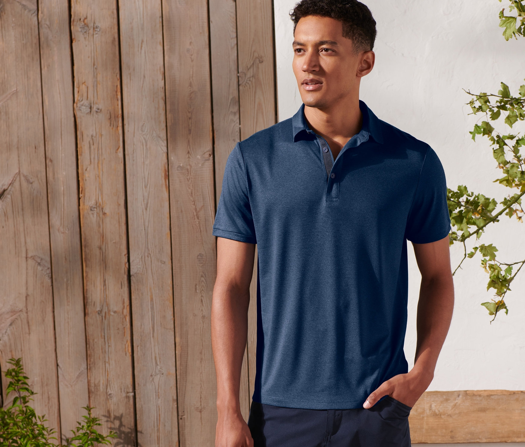 Mann posiert draußen und trägt ein Funktions-Poloshirt.