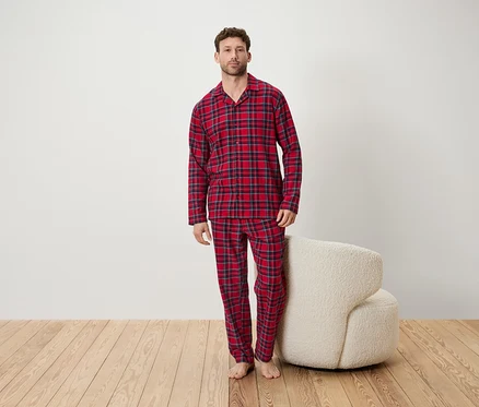 Mann im rot karierten Pyjama steht in einem Raum neben einem weißen Sessel.