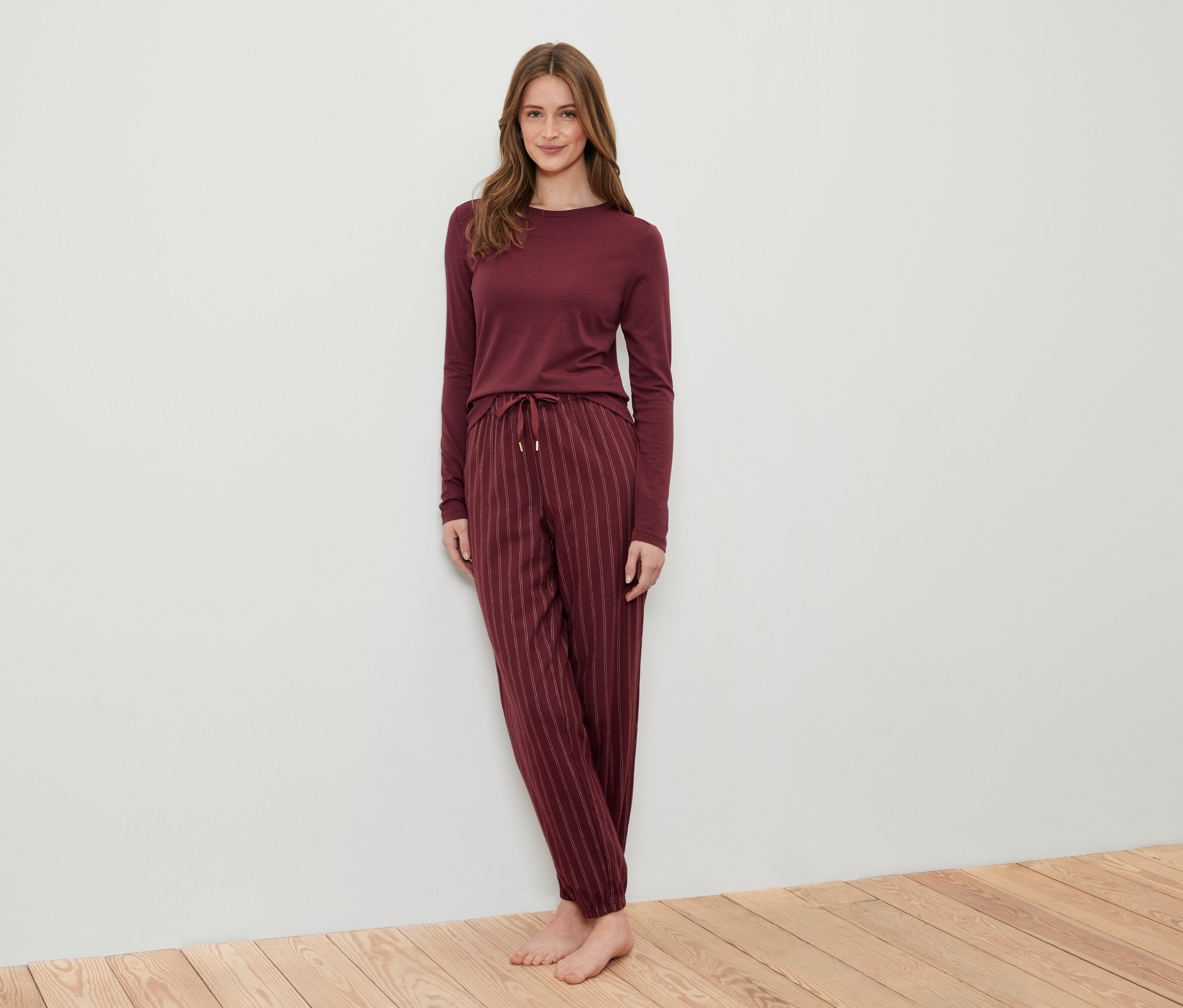 Frau posiert in einem burgunderfarbenen, gestreiften Pyjama auf einem Holzboden.