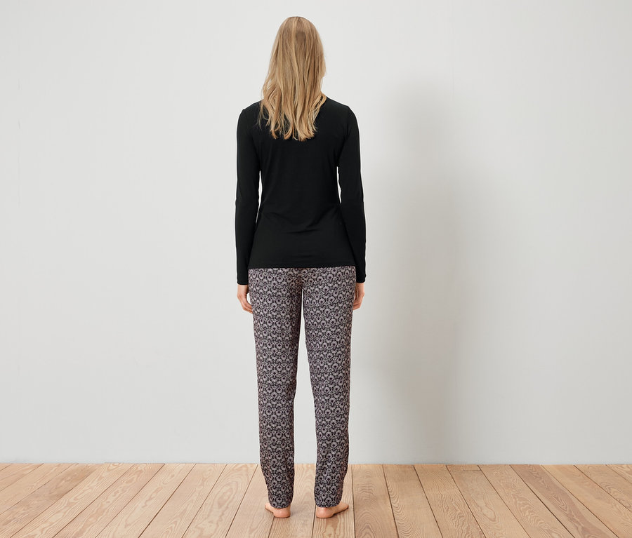 Eine Frau steht mit dem Rücken zur Kamera und trägt ein schwarzes Langarmshirt und gemusterte Hosen.