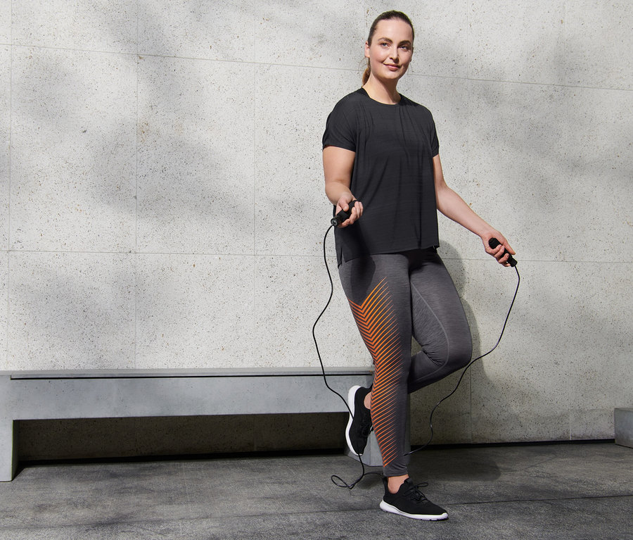 Frau mit Sporttight, schwarz mit Print und Sportshirt, schwarz meliert springt Seil.