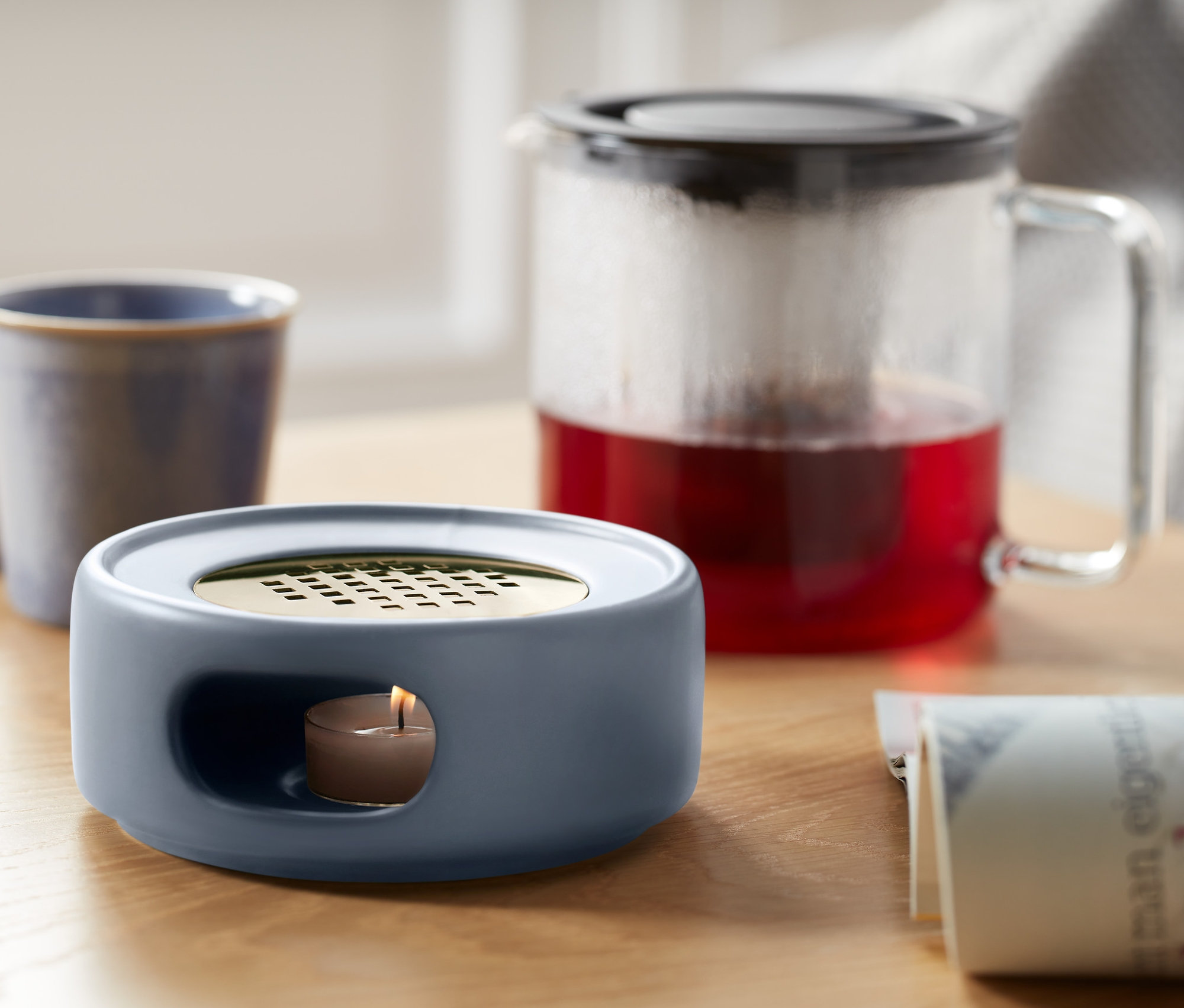 Auf einem Tisch stehen ein Stövchen, eine Tasse und eine Teekanne.