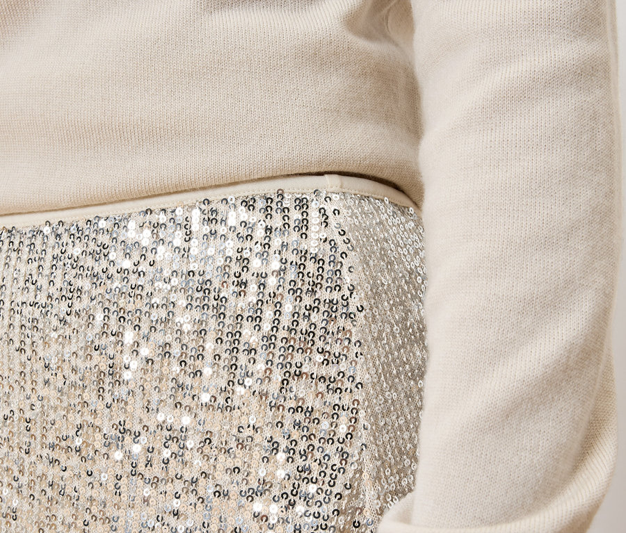 Detail eines Damenoutfits: cremefarbener Pullover und silberner Paillettenrock.