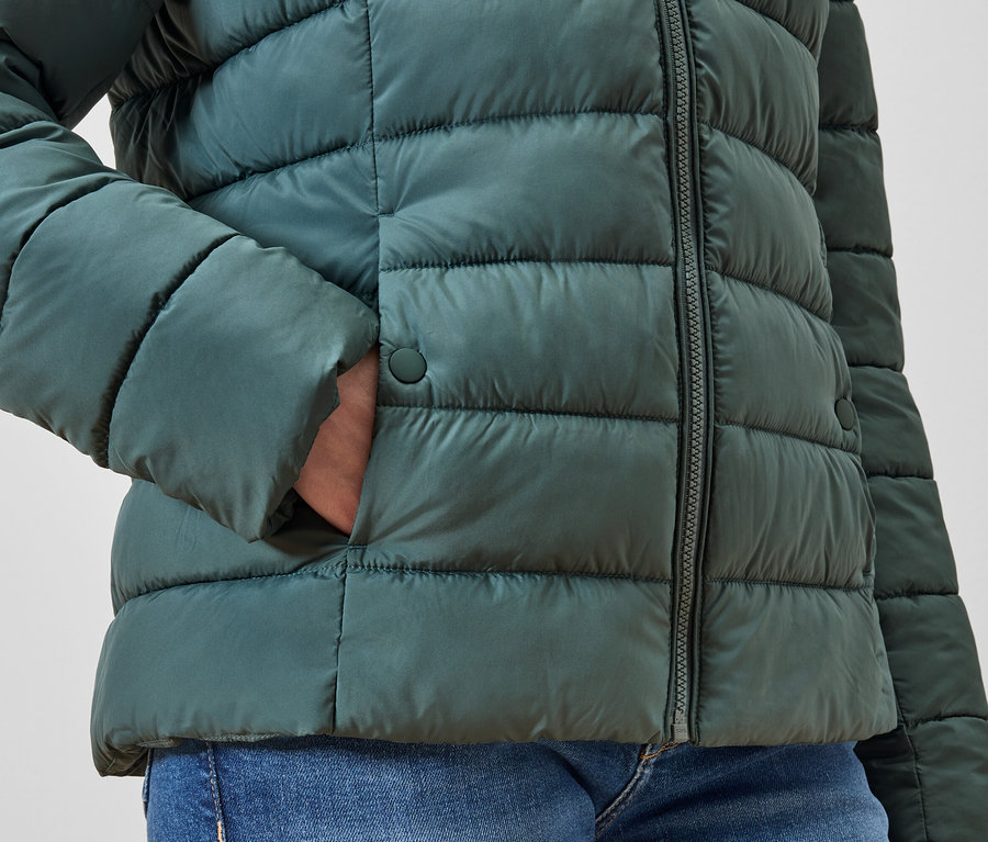 Hand in der Tasche einer grünen Steppjacke.