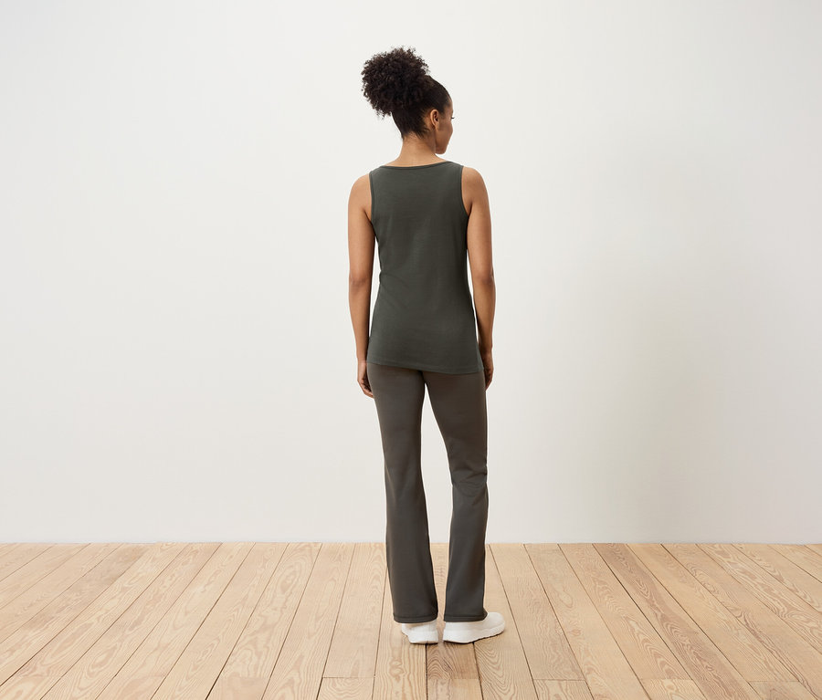 Frau steht mit dem Rücken zur Kamera, trägt ein Tanktop und Hosen.