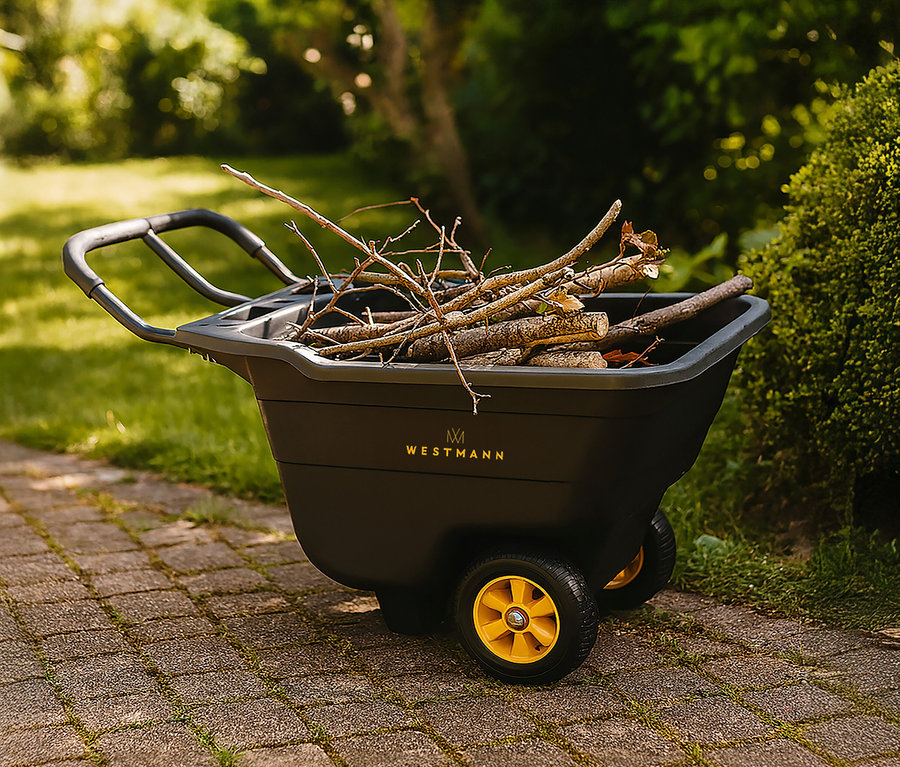 Eine schwarze Schubkarre mit gelben Rädern, gefüllt mit Ästen, steht auf einem gepflasterten Weg.