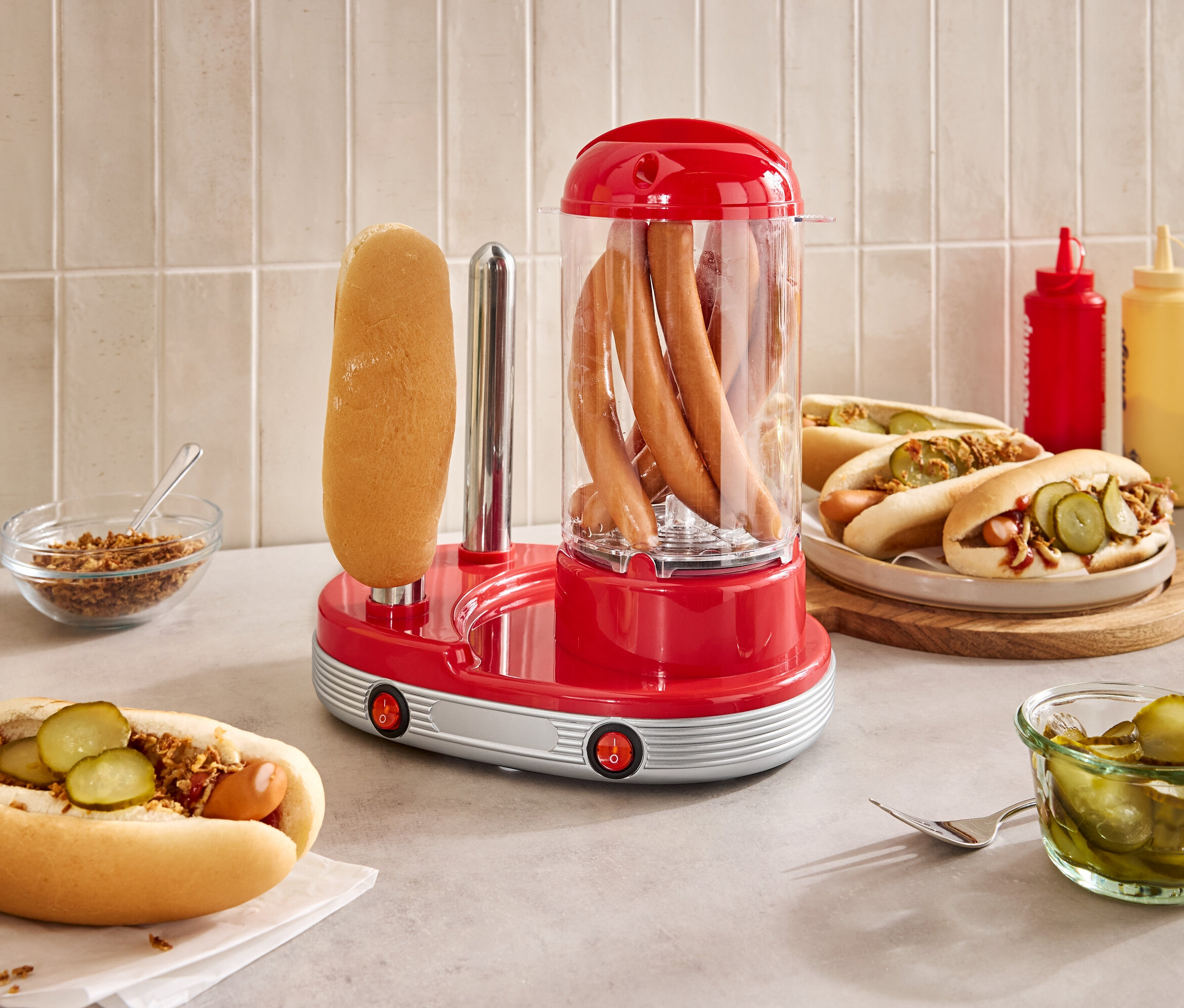 Auf einer Theke steht ein roter Hot-Dog-Maker mit Würstchen drin und einem Brötchen außen.