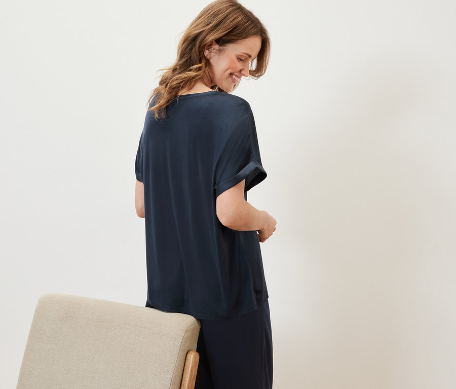 Frau schaut nach unten und trägt ein marineblaues Blusenshirt im Materialmix und eine dunkelblaue Hose.