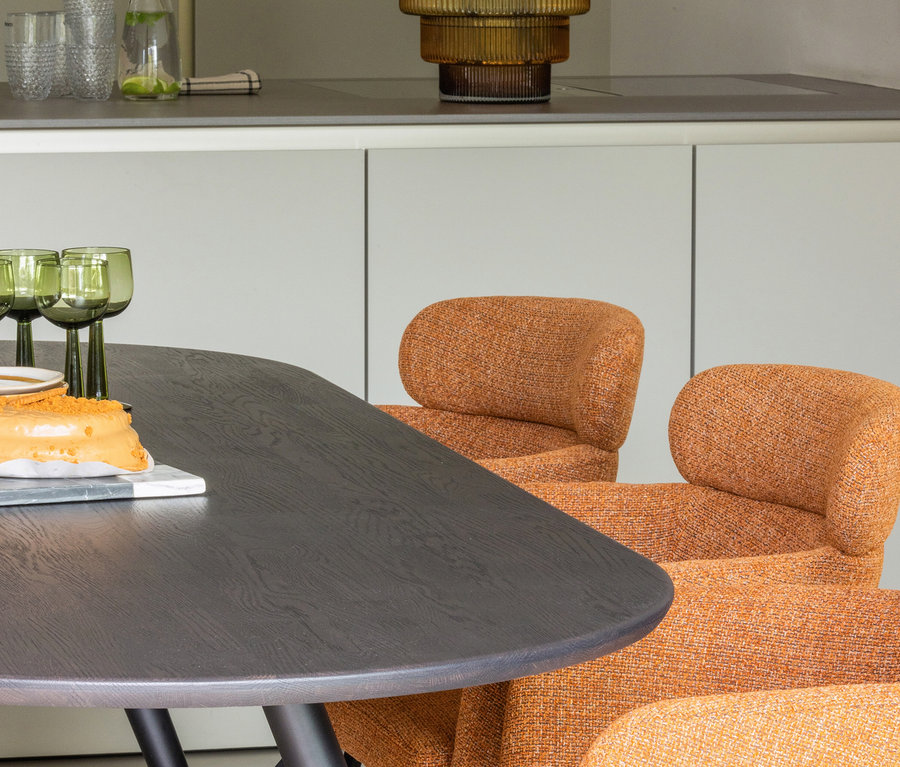 Auf dem Tisch stehen ein Kuchen und grüne Gläser, im Hintergrund zwei orangefarbene Woood Stühle »Fenne«.
