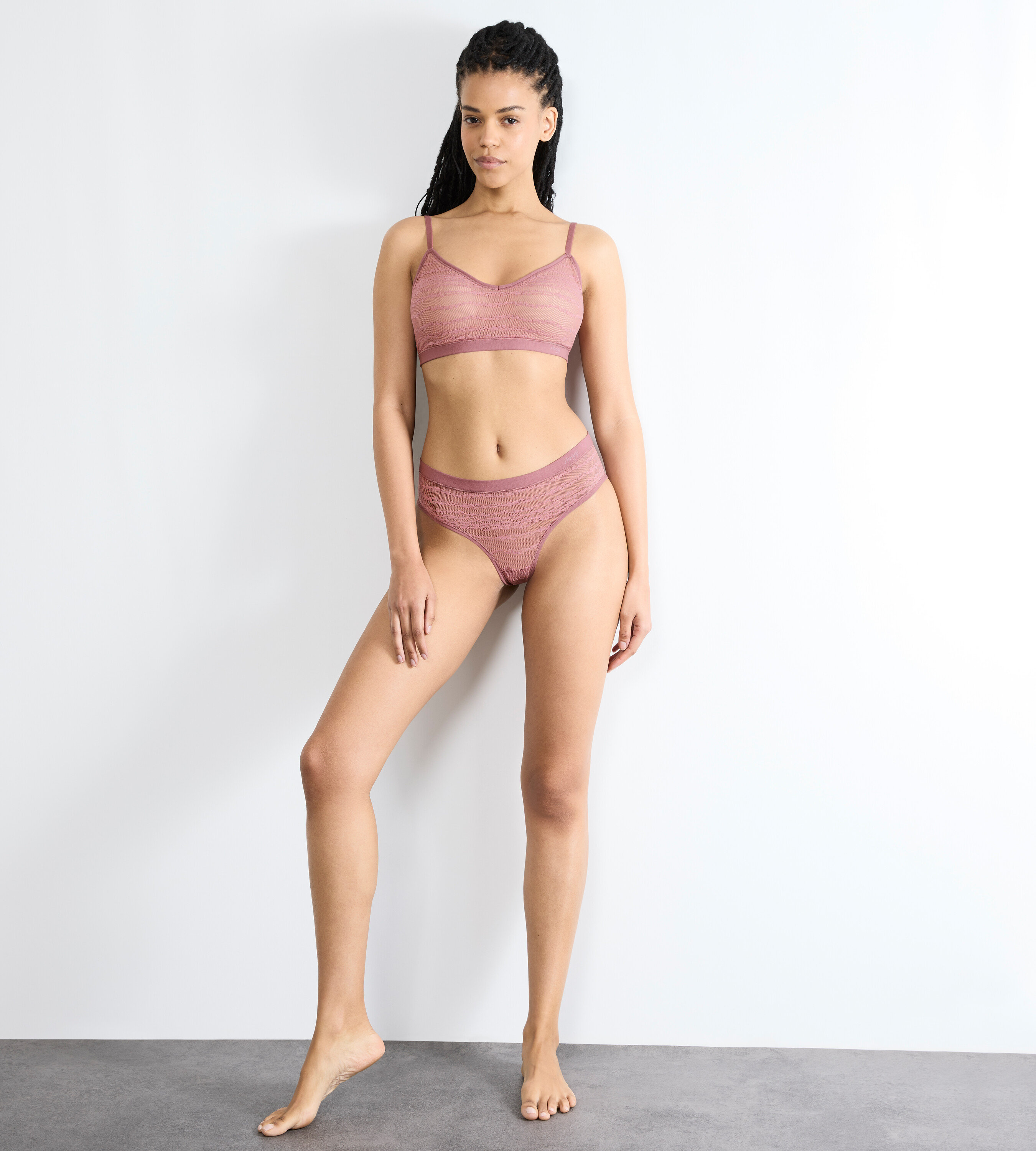 Frau posiert in einem rosa Unterwäsche-Set vor einer weißen Wand.