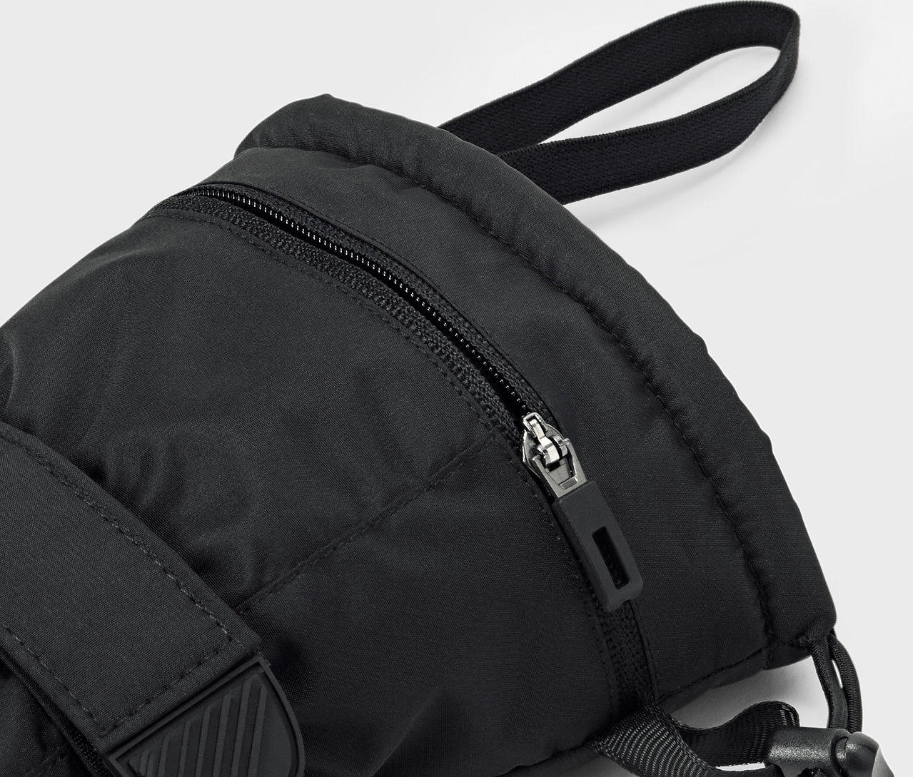 Detailaufnahme eines schwarzen Rucksacks mit Reißverschluss und Tragegurt.