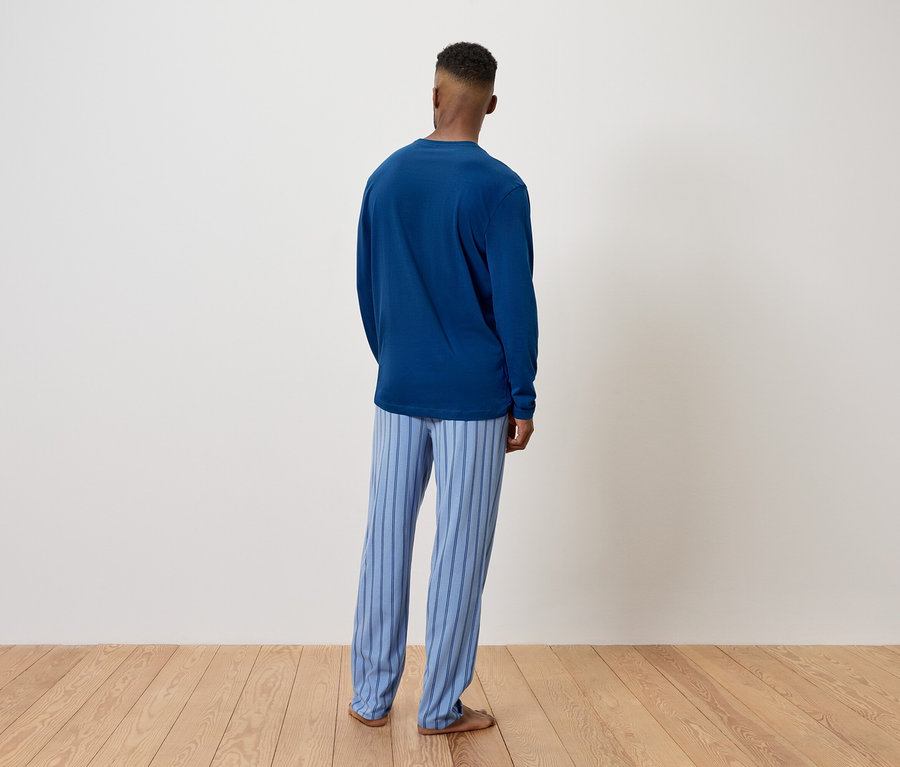 Mann in blauem Pullover und gestreifter Hose steht mit dem Rücken zur Kamera.