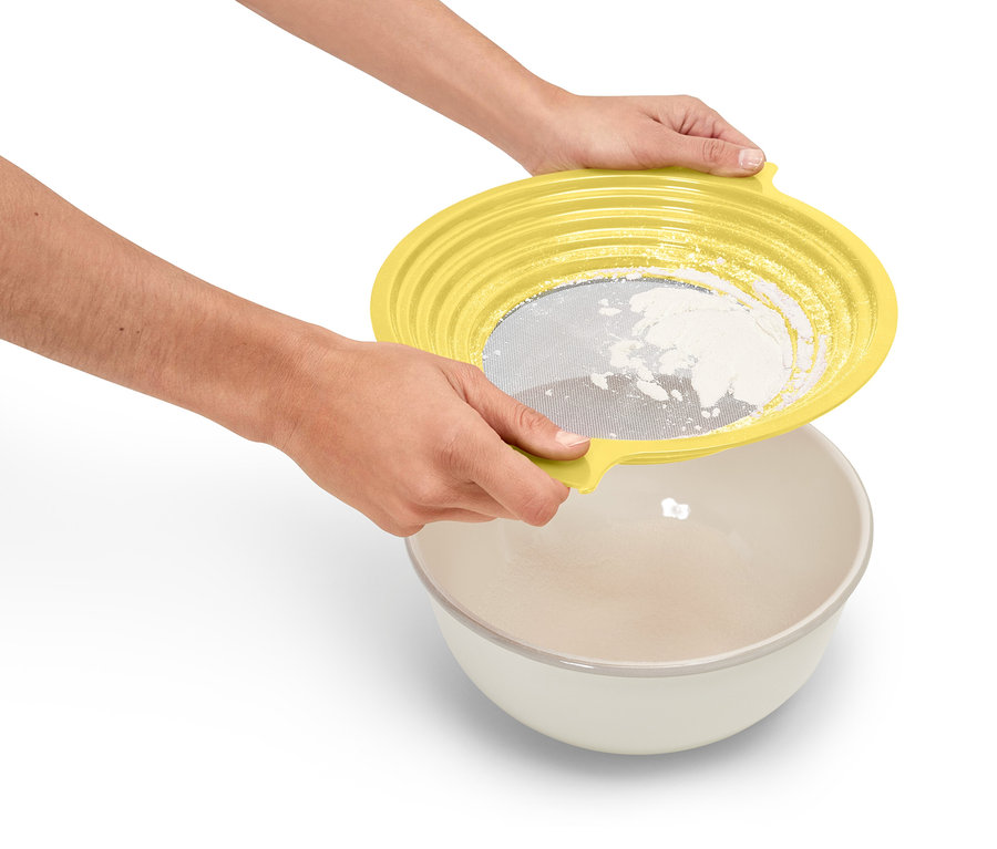 Person hält gelbes Sieb über eine Schüssel und siebt Mehl.