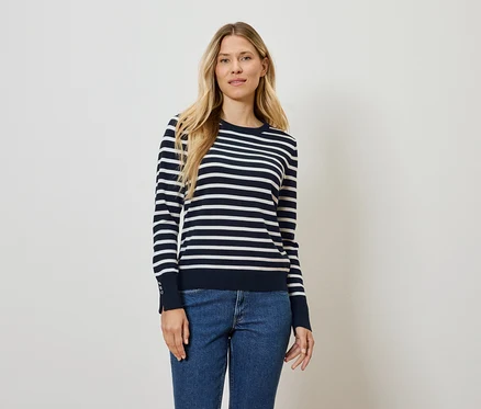 Frau steht und posiert in einem blau-weiß gestreiften Pullover und Jeans.