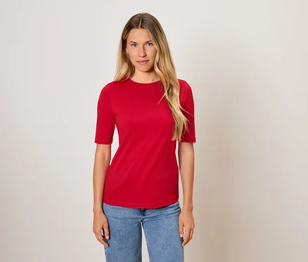Frau mit langen blonden Haaren posiert in einem roten T-Shirt und blauen Jeans.