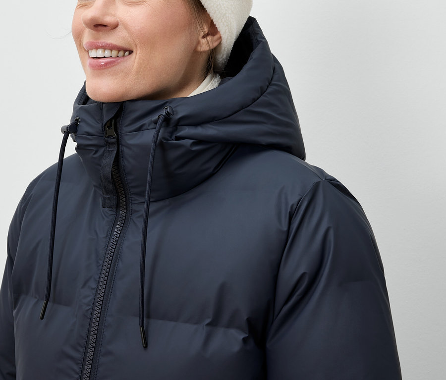 Frau trägt eine dunkelblaue Daunenjacke und eine weiße Mütze.
