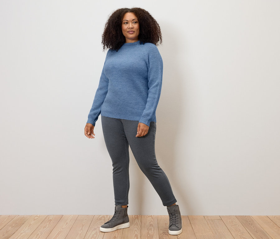 Frau steht auf Holzboden und trägt blauen Pullover und graue Stoffhose mit Hahnentritt-Jacquard.