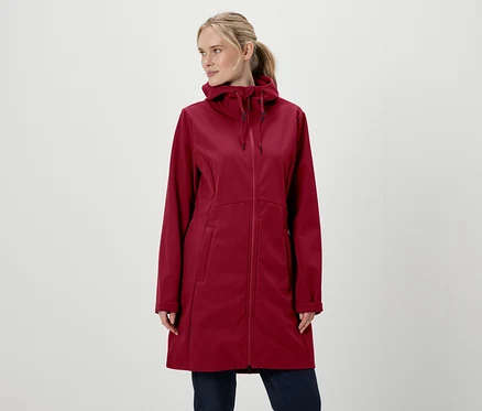Blonde Frau in weinroter Kapuzenjacke mit Reißverschluss und Hose vor weißem Hintergrund.