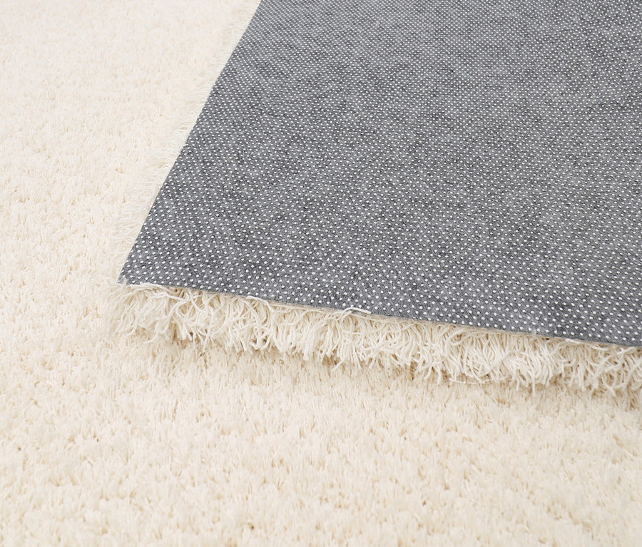 Nahaufnahme eines Teppichs »Pleasure« in Creme, teilweise umgeklappt, um die Unterseite zu zeigen.