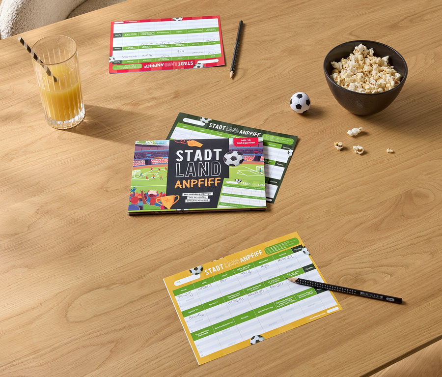 Auf einem Holztisch liegen Spielblöcke, ein Glas Orangensaft mit Strohhalm, eine Schüssel Popcorn und ein kleiner Fußball.