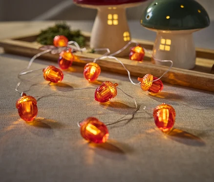 Nahaufnahme von Eichel-Lichterkette auf Tisch neben Pilzlampen auf Holztablett.