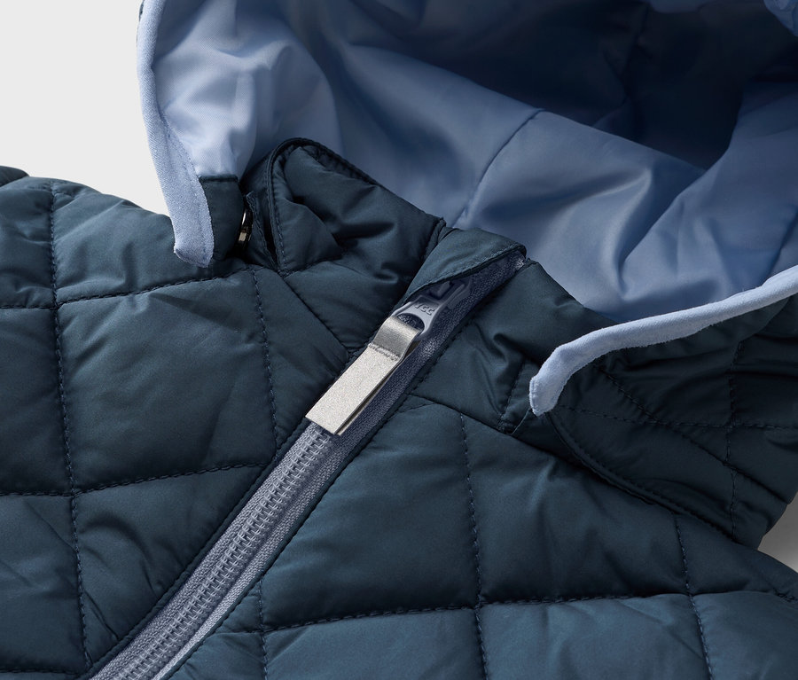 Nahaufnahme einer gesteppten, marineblauen Jacke mit hellblauem Innenfutter und silbernem Reißverschluss.