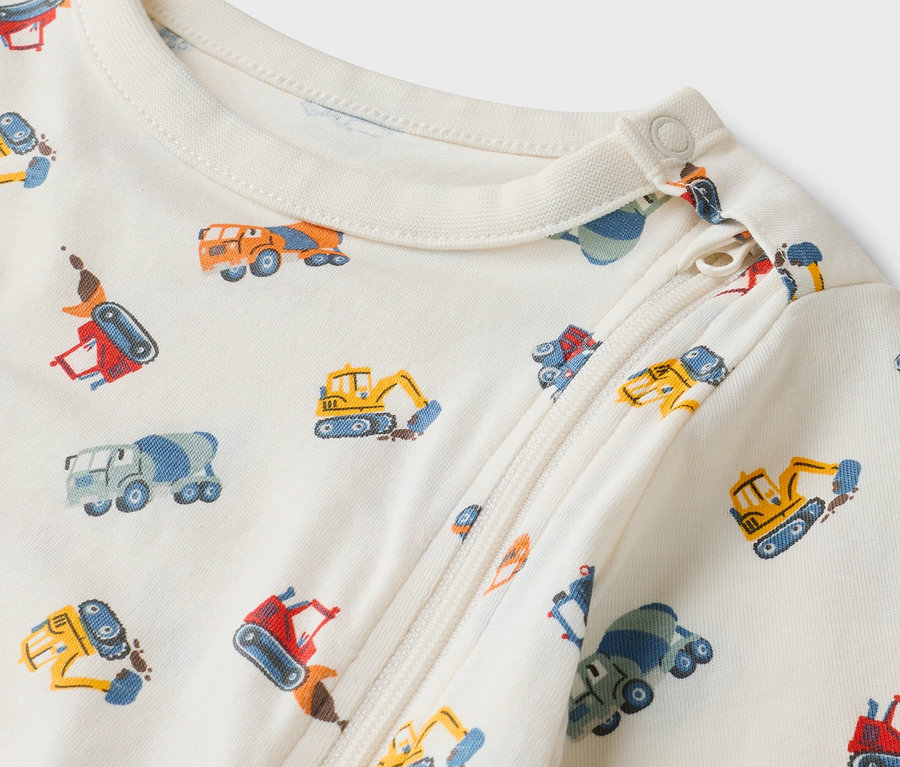 Nahaufnahme eines cremefarbenen Baby-Schlafanzugs mit Reißverschluss und Bauwagenmuster.