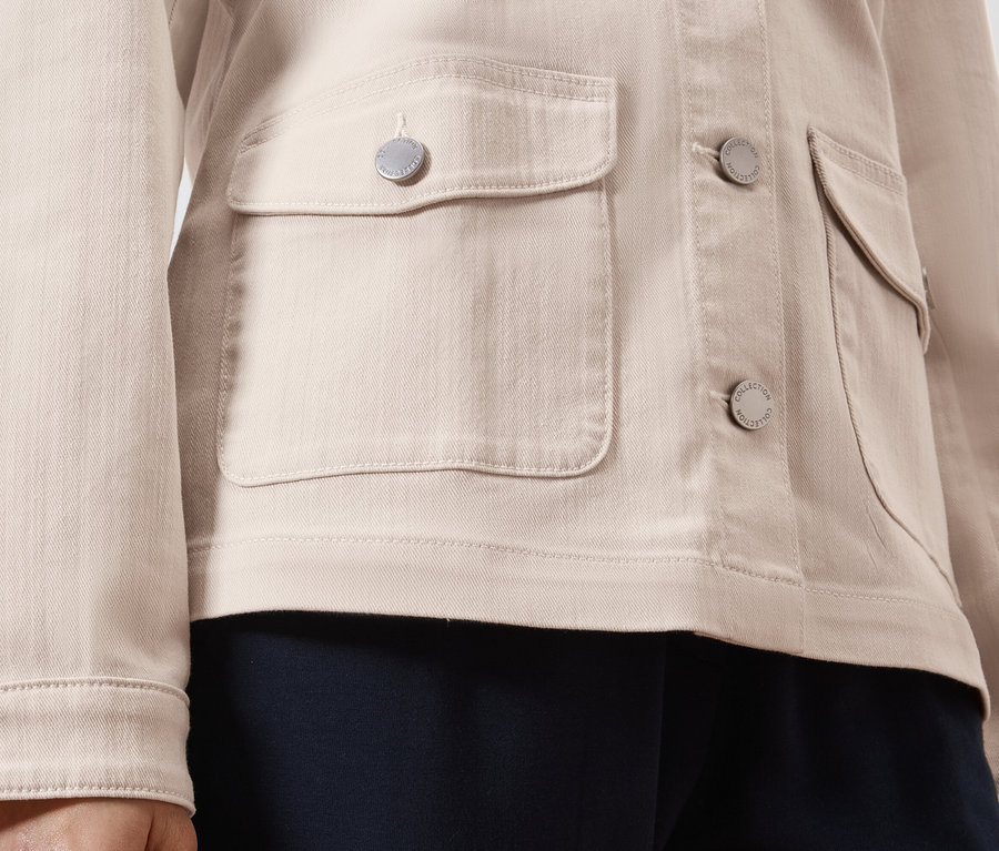 Nahaufnahme einer hellbraunen Jeansjacke mit silbernen Knöpfen und aufgesetzten Taschen.