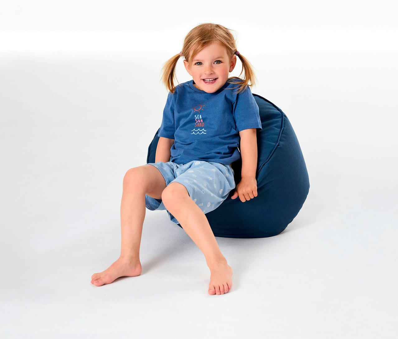 Mädchen sitzt auf einem Sitzsack und trägt einen kurzen Kinderpyjama von SCHIESSER.