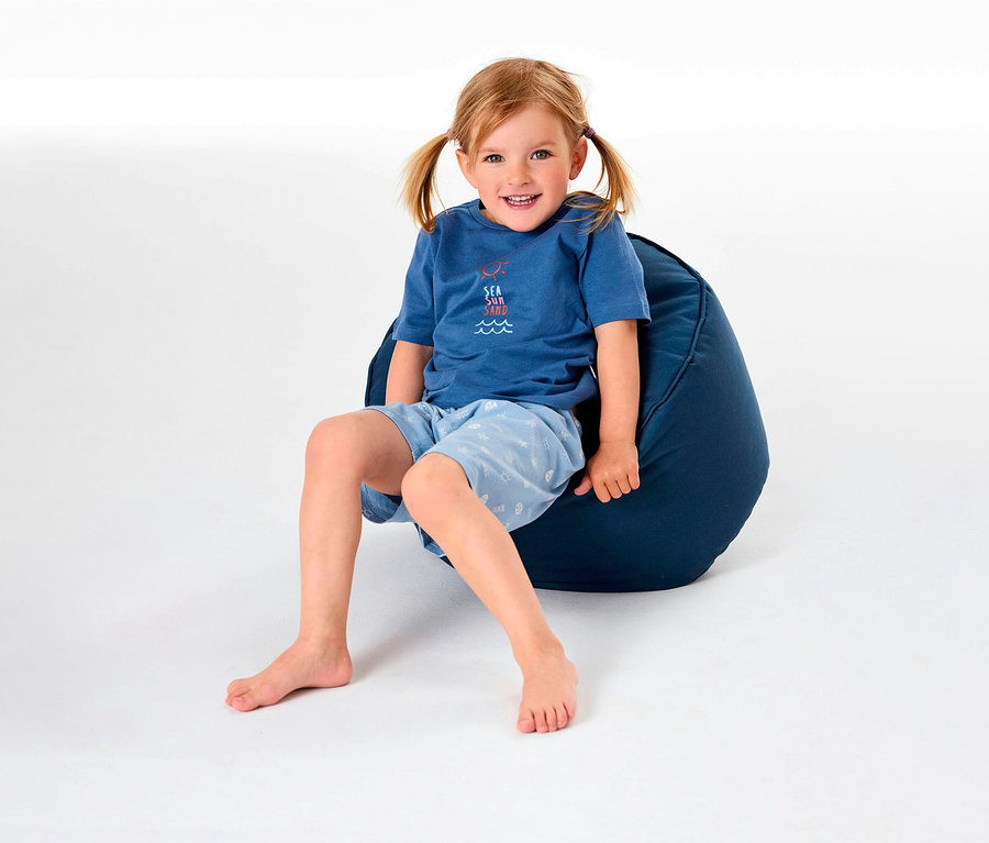 Mädchen sitzt auf einem Sitzsack und trägt einen kurzen Kinderpyjama von SCHIESSER.
